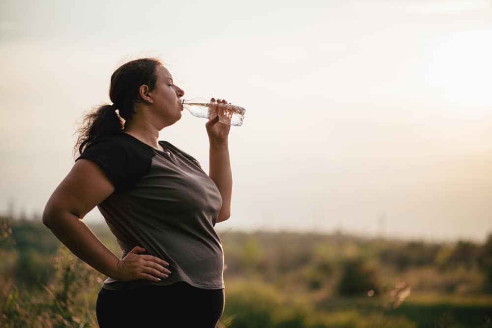 Plus-sized woman outside, drinking water during workout for weight loss.