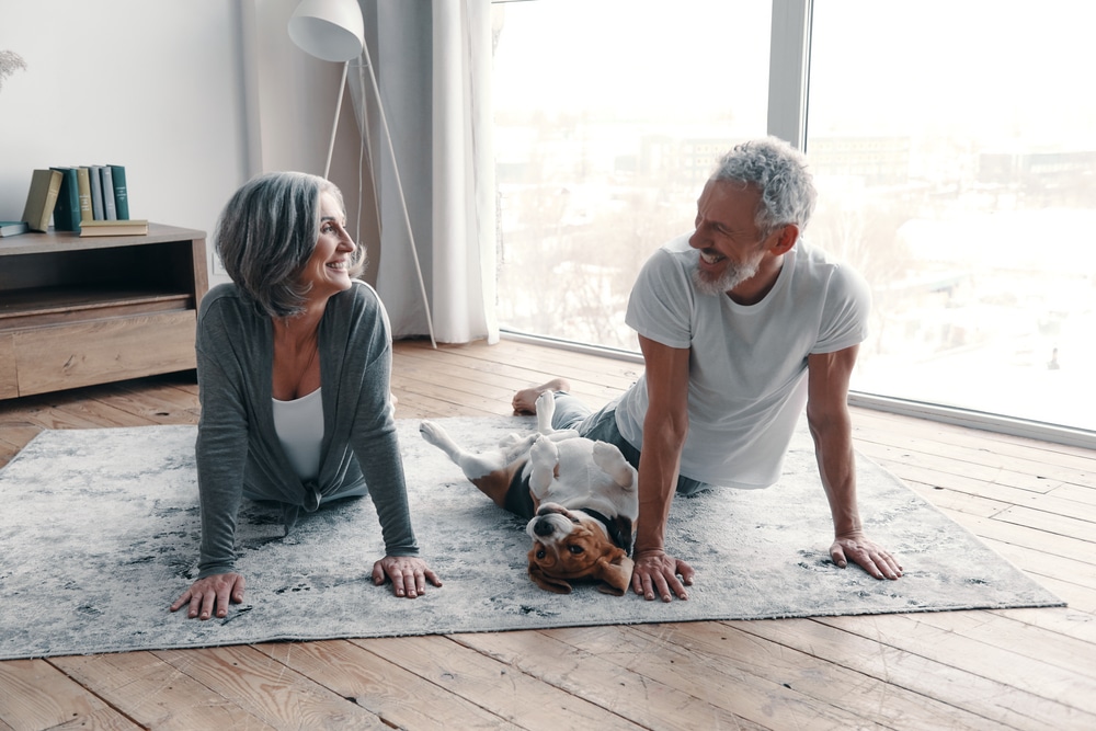 Older couple doing yoga on the ground as a healthy aging strategy, and smiling at each other
