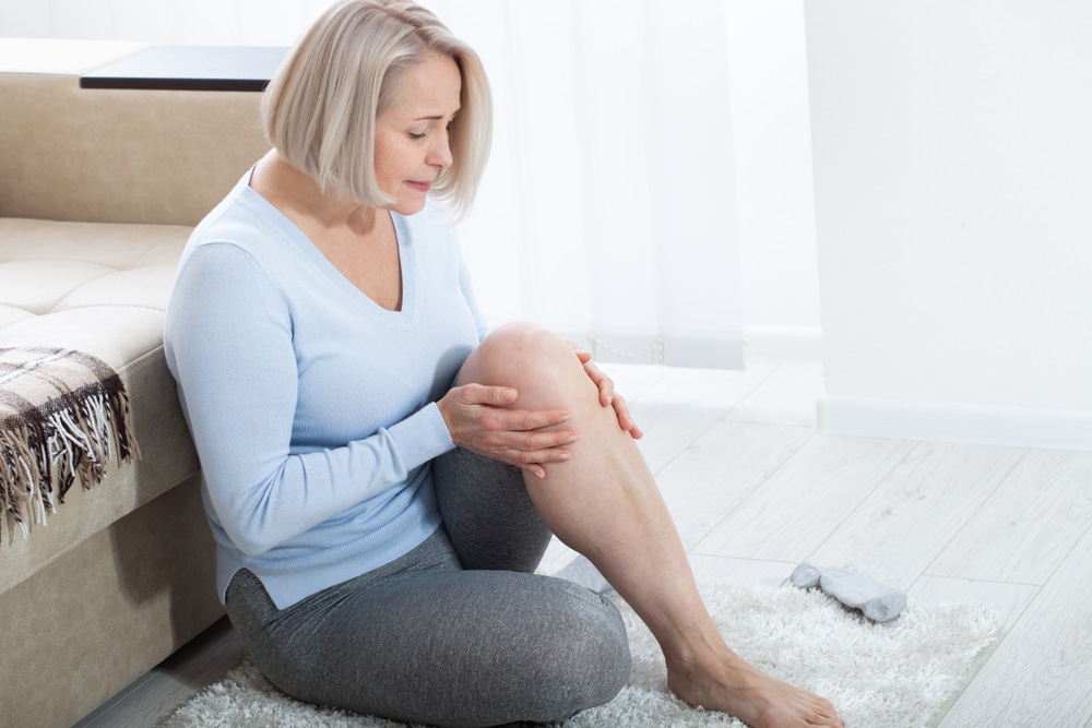 Woman in 50s sitting and holding her knee experiencing joint pain due to menopausal changes