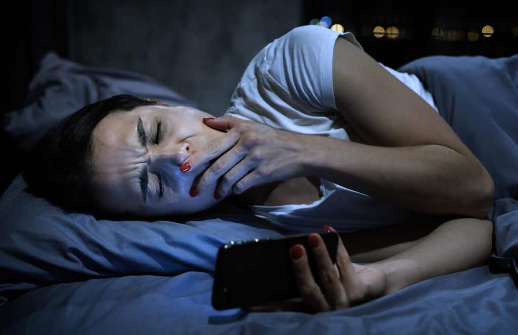 Woman awake at night checking her phone after interrupted sleep.