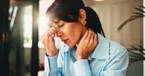 Woman holding her neck and forehead while experiencing fatigue and discomfort
